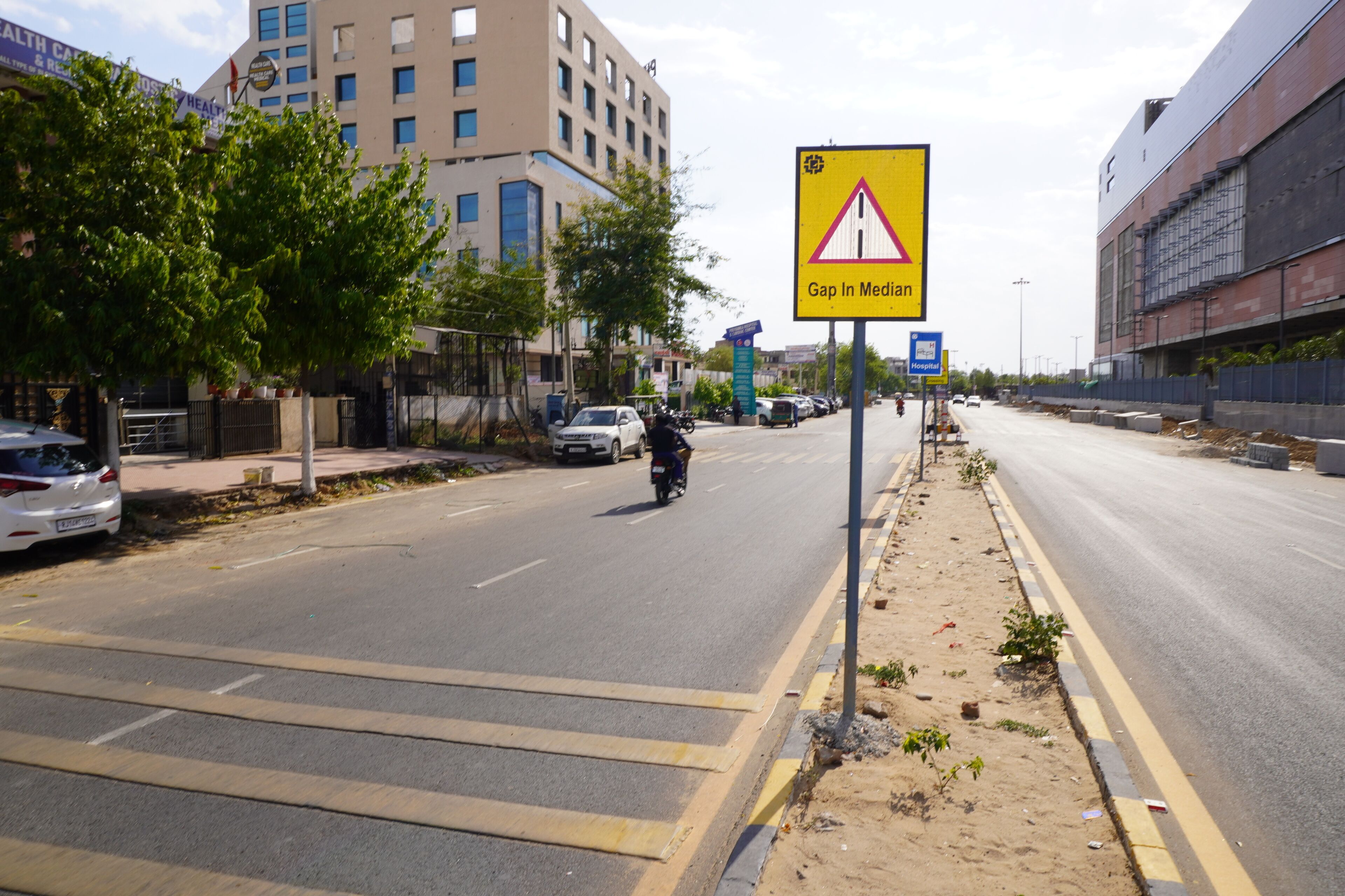 A road with a 'Gap In Median' sign, a motorcyclist, and buildings in the background.