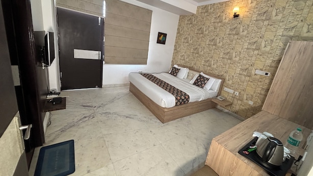 A bedroom with a bed, bedside table, and a small desk with a kettle. - Hotel Sun Heritage (Jaipur)