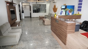 A reception area with a wooden desk, a sofa, a television, and a large window. - Hotel Sun Heritage (Jaipur)