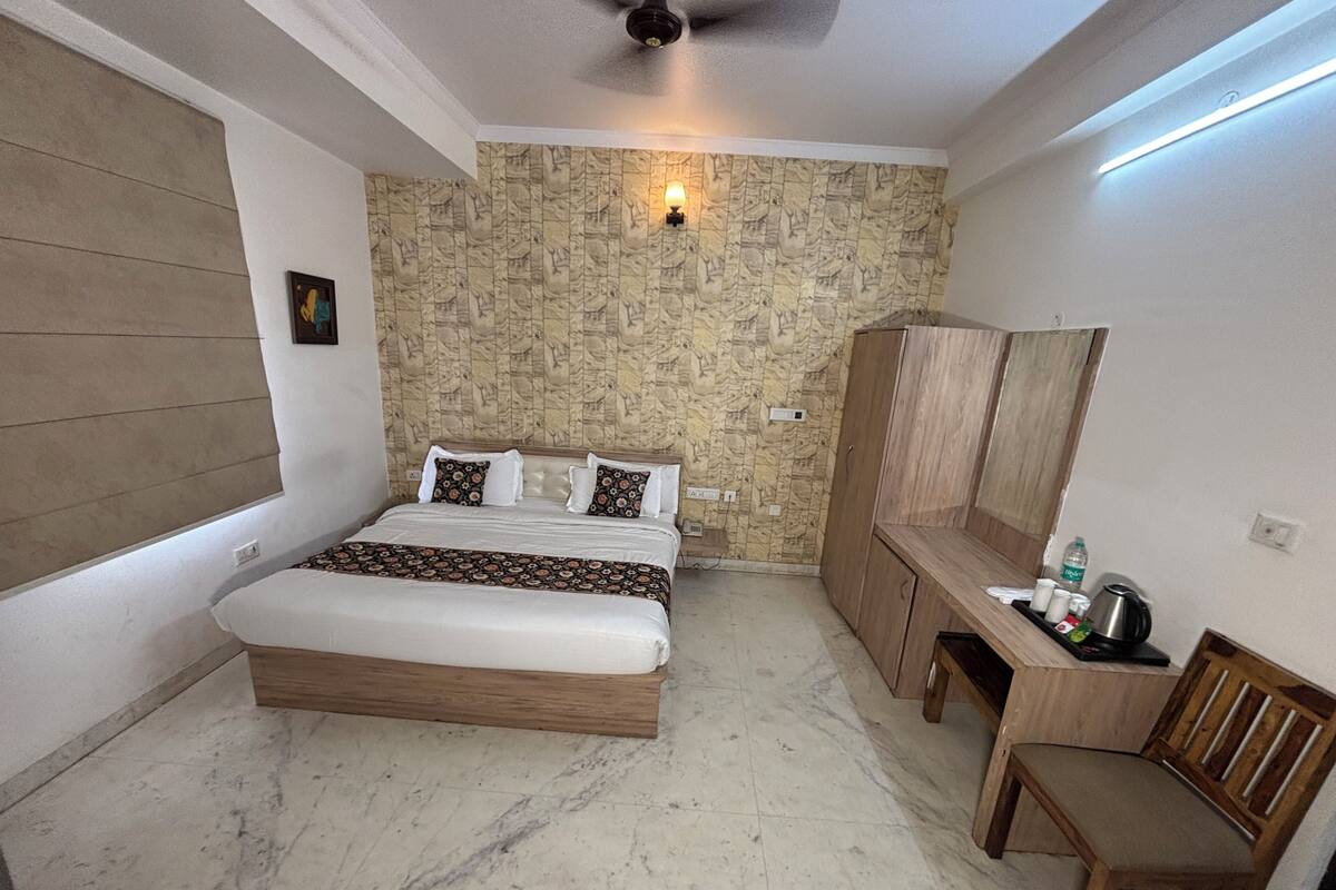 A bedroom with a bed, a wooden wardrobe, a desk with a chair, and a wall-mounted light.