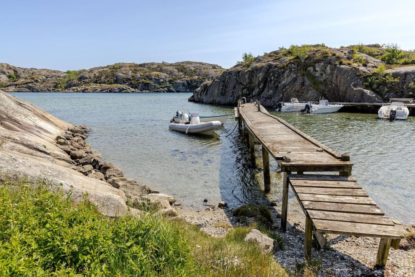 Une jetée en bois s’étendant dans une étendue d’eau calme, entourée d’un terrain rocheux et d’une végétation clairsemée.