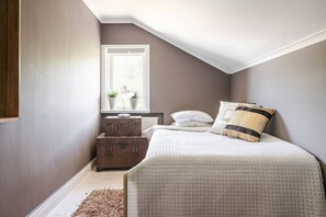 A bedroom with a sloped ceiling, a window with plants, a bed with a quilted cover, and a wooden chest of drawers. - Elegant 8BR Mansion Retreat (Delsbo)
