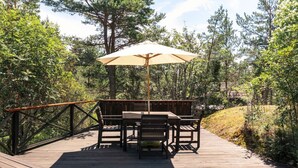 Una terraza de madera con una mesa, sillas, una sombrilla y una barandilla.
