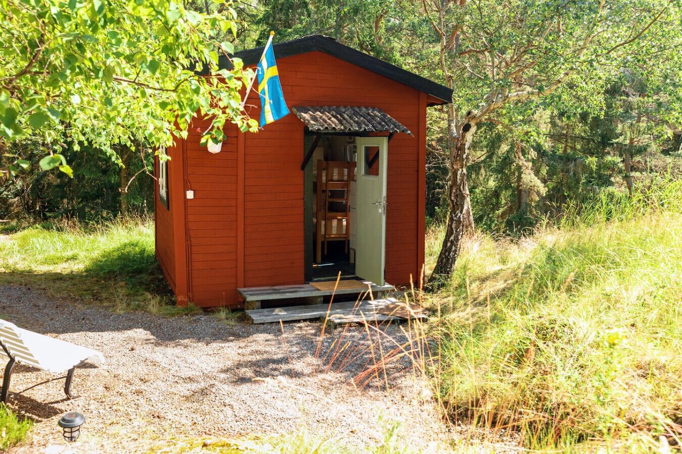 Una pequeña cabaña de madera con la puerta abierta, rodeada de árboles y césped.