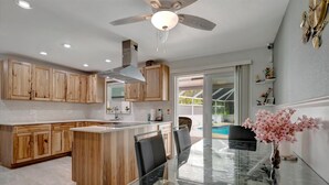 Ett modernt kök med träskåp, ett matbord i glas och en takfläkt.