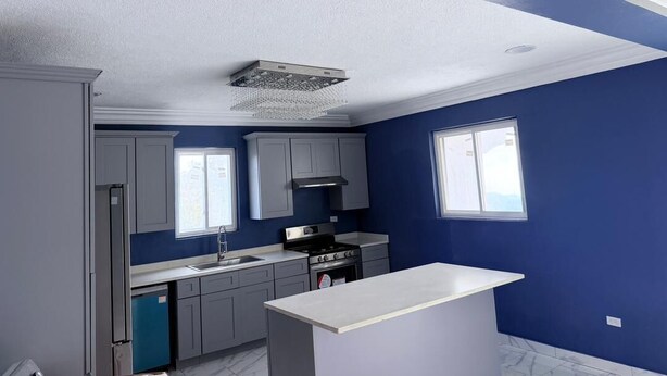 Una cocina con armarios grises, encimera blanca, estufa y ventana.