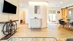 Un salon moderne doté d’un téléviseur à écran plat, d’un meuble blanc et d’un coin repas avec une table et des chaises.
