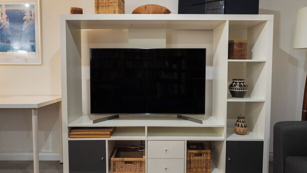 Una sala de estar moderna con televisor de pantalla plana, estanterías empotradas, cestos de mimbre y un cuadro en la pared.