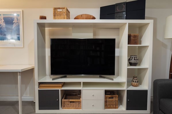 A modern living room with a flat-screen TV, built-in shelving, wicker baskets, and a framed picture on the wall.