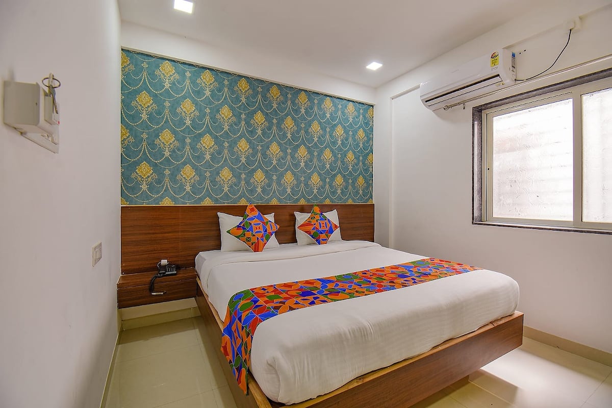 A bedroom with a bed, a nightstand, a wall-mounted air conditioner, and a window.
