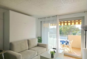 A modern living room with a sofa, a coffee table with a plant, and a balcony with a table and chairs. - Alyoné : Studio prémium (Antibes)