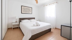 A bedroom with a bed, a nightstand, a desk, a ceiling fan, a window, and a framed picture on the wall. - Urban Riviera (Nice)