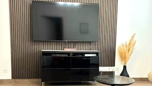 A living room with a flat-screen TV mounted on a wall, a black entertainment unit, a round black coffee table, and a vase with dried pampas grass. - Urban Riviera (Nice)