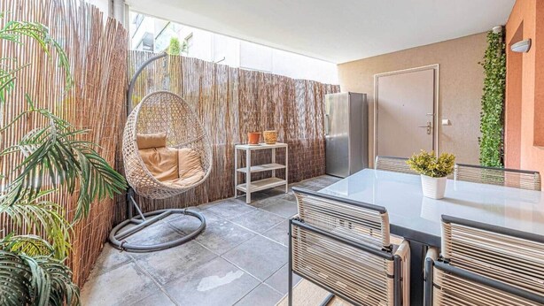 A patio area with a hanging chair, a table with chairs, a refrigerator, and a bamboo fence. - Urban Riviera (Nice)