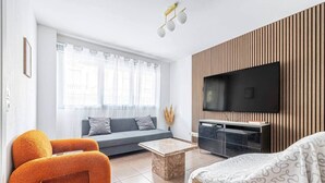 A modern living room with a sofa, orange armchairs, a coffee table, and a TV mounted on a wooden wall. - Urban Riviera (Nice)