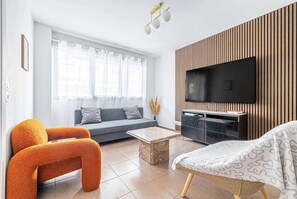 Ein modernes Wohnzimmer mit einer Couch, orangefarbenen Sesseln, einem Couchtisch und einem an einer Holzwand montierten Fernseher.