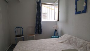 A bedroom with a bed, two chairs, a window with curtains, a lamp, and a mirror on the wall. - PAVILLON T 2 RENOVE 4PERS VAUX SUR MER TERASSE PARKING PISCINE COLLEC COMM ETC (Vaux-sur-Mer)