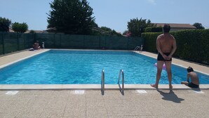 A rectangular swimming pool with a tiled deck, metal ladder, and a safety sign. - PAVILLON T 2 RENOVE 4PERS VAUX SUR MER TERASSE PARKING PISCINE COLLEC COMM ETC (Vaux-sur-Mer)