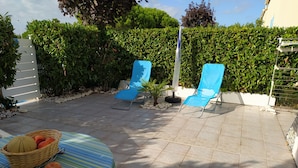 A patio with two blue lounge chairs, a table with a striped tablecloth, and a basket of fruits. - PAVILLON T 2 RENOVE 4PERS VAUX SUR MER TERASSE PARKING PISCINE COLLEC COMM ETC (Vaux-sur-Mer)