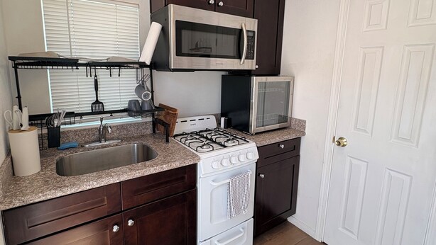 A kitchen with a gas stove, microwave, sink, and dark wooden cabinets.