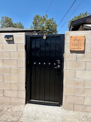 A black metal gate with a house-shaped plaque reading '13225 casita' on a beige brick wall.