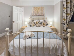 A neatly made bed with a metal headboard, two bedside tables with lamps, a door, and a floral curtain. - Gorgeous house in a great location for exploring East Kent at its finest. (Ramsgate)