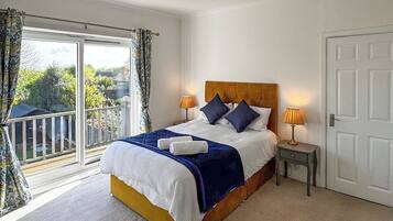 A bedroom with a bed, two bedside lamps, a door, and a balcony with curtains.