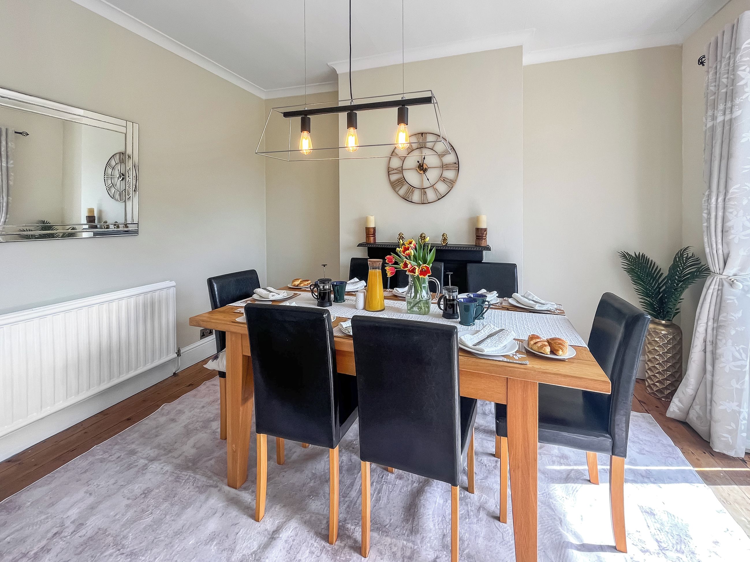 Un coin repas avec une table en bois, des chaises noires, un lustre et une horloge murale.