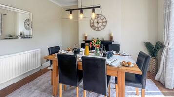 A dining area with a wooden table, black chairs, a chandelier, and a wall clock.