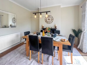 A dining area with a wooden table, black chairs, a chandelier, and a wall clock.