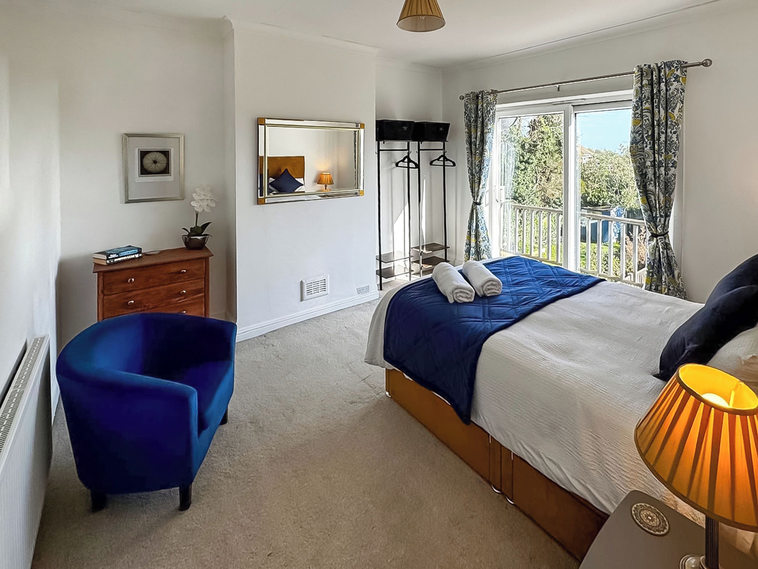 A bedroom with a bed, a dresser, a chair, a mirror, a window with curtains, and a lamp.