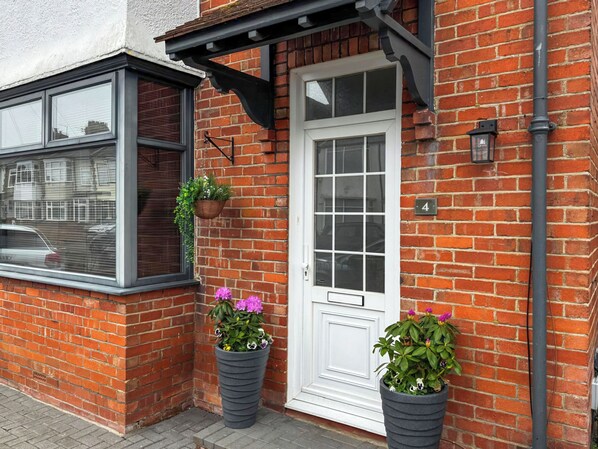 A red brick house with a white door, a window, and two potted plants.