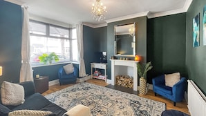 Un salon comprenant un canapé, un fauteuil bleu, une cheminée, un miroir et un lustre.