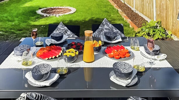Une table à manger d’extérieur, agrémentée de bols, d’assiettes et de verres aux motifs noirs et blancs, entourée de chaises avec des coussins assortis.