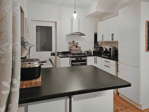 A modern kitchen with white cabinets, a black countertop, and a hanging light fixture.