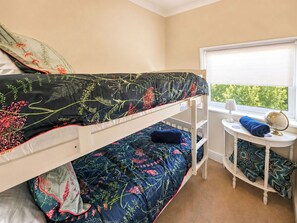 A bunk bed room with a window, a small table with a globe and lamp, and a patterned bedspread.