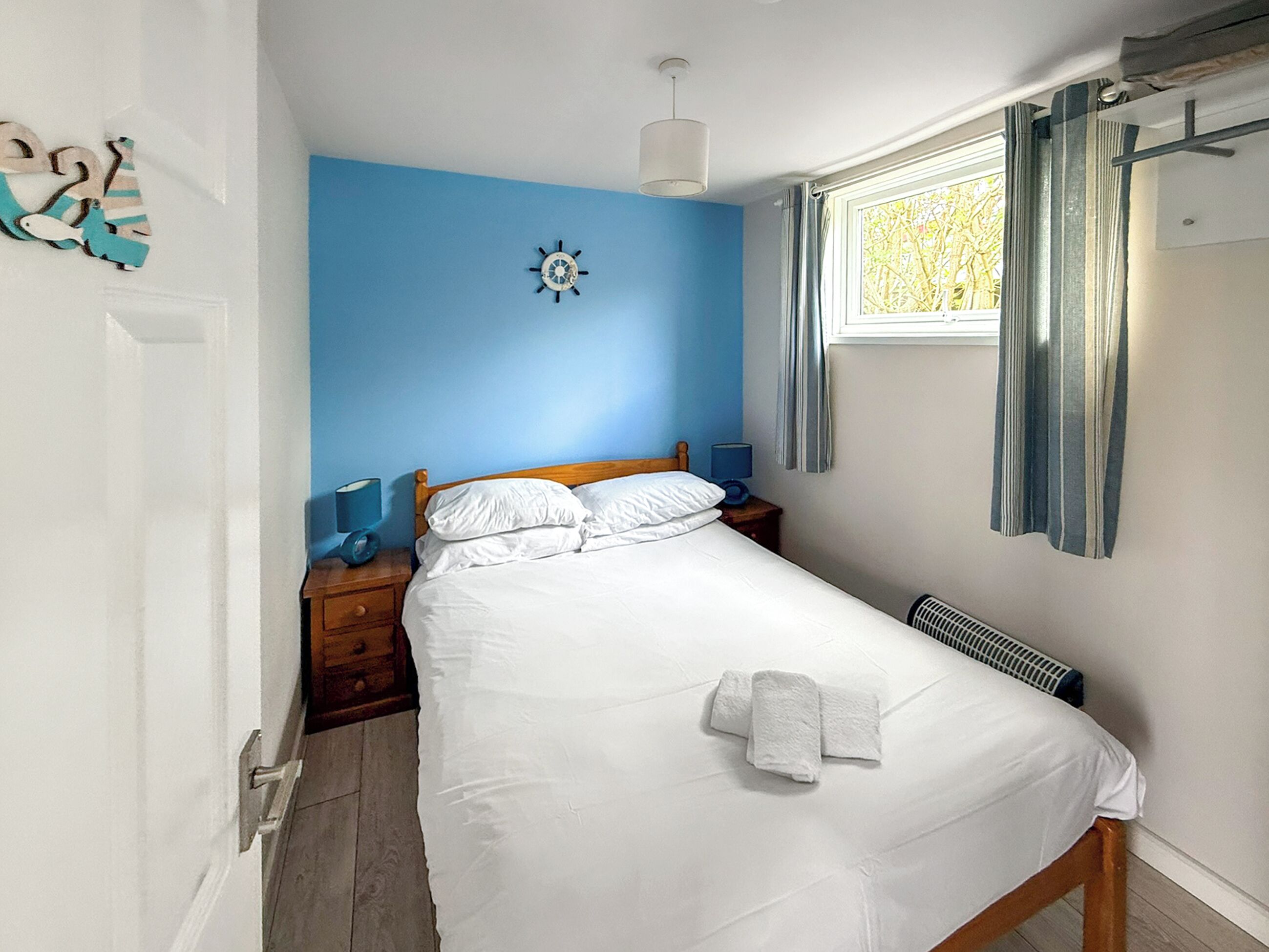 A bedroom with a bed, a nightstand, a wall clock, a window with curtains, and a radiator.