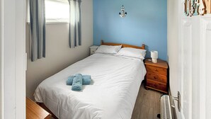 Et soveværelse med en seng, et natbord, en lampe og et vindue med gardiner.
