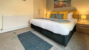 Quarto com cama, abajures, radiador, tapete e obras de arte nas paredes.