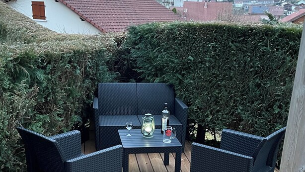 Eine Holzterrasse mit Korbmöbeln, einem Tisch und einer Karaffe.