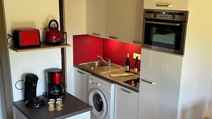 Eine kompakte Küche mit Waschmaschine, Kaffeemaschine, Toaster und einer Weinflasche.