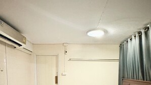 A hotel room with a bed, a wooden headboard, a ceiling light, a window with curtains, and a door. - Prompt Inn Chareonkrung (Bangkok)