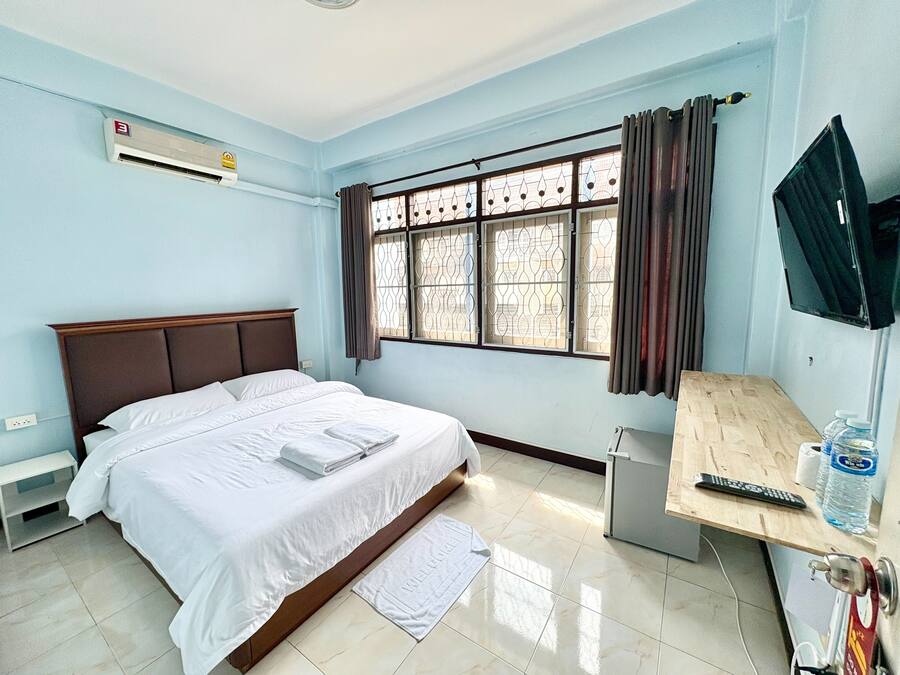 Habitación de hotel con cama, televisión, escritorio, dispensador de agua y ventana con cortinas.