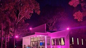 Una casa moderna con fachada de vidrio, un espacio exterior para sentarse a la vista y una entrada bien iluminada.