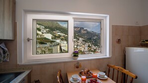 A kitchen with a view of a hillside town, a dining table with breakfast, and a refrigerator. - The Seagull - Tradewinds (Praiano)