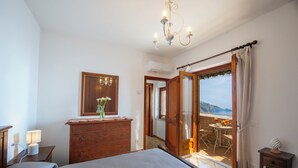 A bedroom with a bed, dresser, mirror, and a view of a balcony with outdoor furniture. - The Seagull - Tradewinds (Praiano)