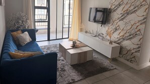 Moderni olohuone, jossa on sininen sohva, litteänäyttöinen televisio, valkoinen tv-taso ja marmorikuvioitu seinä.