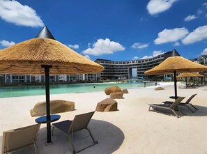 Un complexe hôtelier doté d’une piscine, de chaises longues et de parasols en chaume.