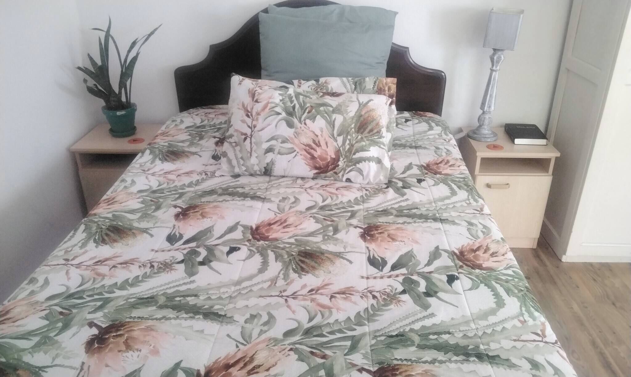 Ein Bett mit floraler Bettwäsche, eine Nachttischlampe, ein Nachttisch und ein Topfpflanze.