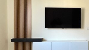 A modern living room with a flat-screen TV mounted on the wall, a wooden accent panel, and a white cabinet below. - Rome Vatican/ Dimora 63 AIR CONDITIONING & WI-FI Premium Apartment (Roma)